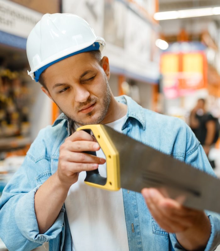 Male customer choosing saw in hardware store